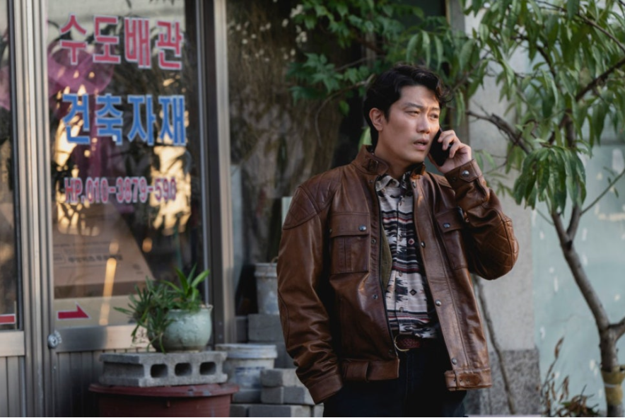 이 스틸컷은 영화 어쩔 수가 없다에서 최선출(박희순)이 캐주얼한 가죽 재킷 차림으로 건축 자재상 앞에서 통화하는 모습을 포착하고 있습니다. 다소 긴장한 듯 보이는 표정으로 전화 통화에 집중하고 있어, 그가 처한 복잡한 상황을 짐작하게 합니다.