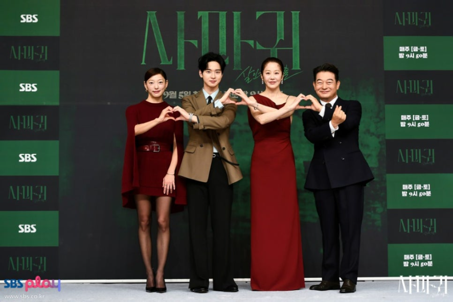 출연진 4명이 어두운 배경 앞에서 밝은 미소를 지으며 손으로 하트 포즈를 만들고 있습니다. 배우들은 버건디/레드 계열의 의상을 중심으로 스타일링했으며, 드라마의 제목('사마귀')과 방영 정보가 배경에 보입니다.