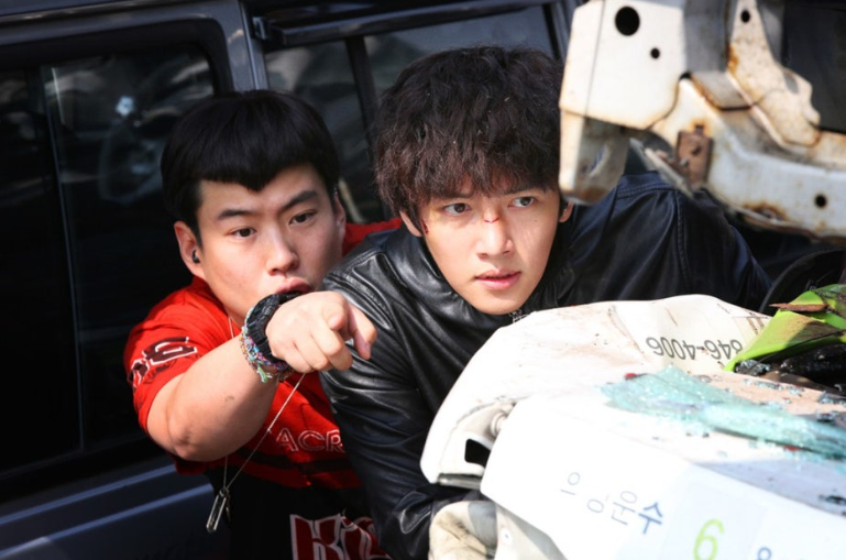 영화 **'조작된 도시'**의 두 인물이 긴박한 상황 속에서 무언가를 주시하는 장면을 담고 있습니다.